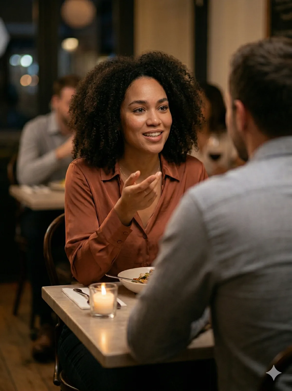 A woman on a date, mid-conversation with a man across a small café table, warm indoor lighting